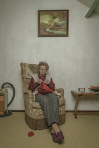 oude vrouw is aan het breien in een antieke stoel met een oude antieke stofzuiger naast de stoel Fotograaf Deventer | Bedrijfsfotografie | Geënsceneerde fotografie | Studiofotografie