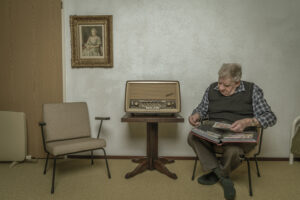 oude man met postzegels zit naast een oude antieke radio met een schilderij aan de muur van koningin elizabeth Fotograaf Deventer | Bedrijfsfotografie | Geënsceneerde fotografie | Studiofotografie
