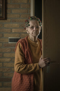 vintage portret van een oude vrouw met krulspelden in haar haar in een deuropening van een oud huis Fotograaf Deventer | Bedrijfsfotografie | Geënsceneerde fotografie | Studiofotografie