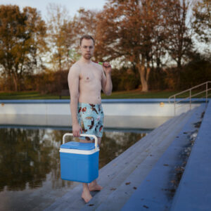 man met een luchtbed bij het zwembad op een koude dag met een glijbaan op de achtergrond Fotograaf Deventer | Bedrijfsfotografie | Geënsceneerde fotografie | Studiofotografie