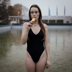 vrouw met een ijsje in haar hand in het zwembad op een koude dag met een glijbaan op de achtergrond Fotograaf Deventer | Bedrijfsfotografie | Geënsceneerde fotografie | Studiofotografie