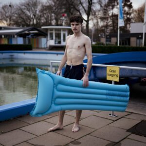 man met een luchtbed bij het zwembad op een koude dag met een glijbaan op de achtergrond Fotograaf Deventer | Bedrijfsfotografie | Geënsceneerde fotografie | Studiofotografie